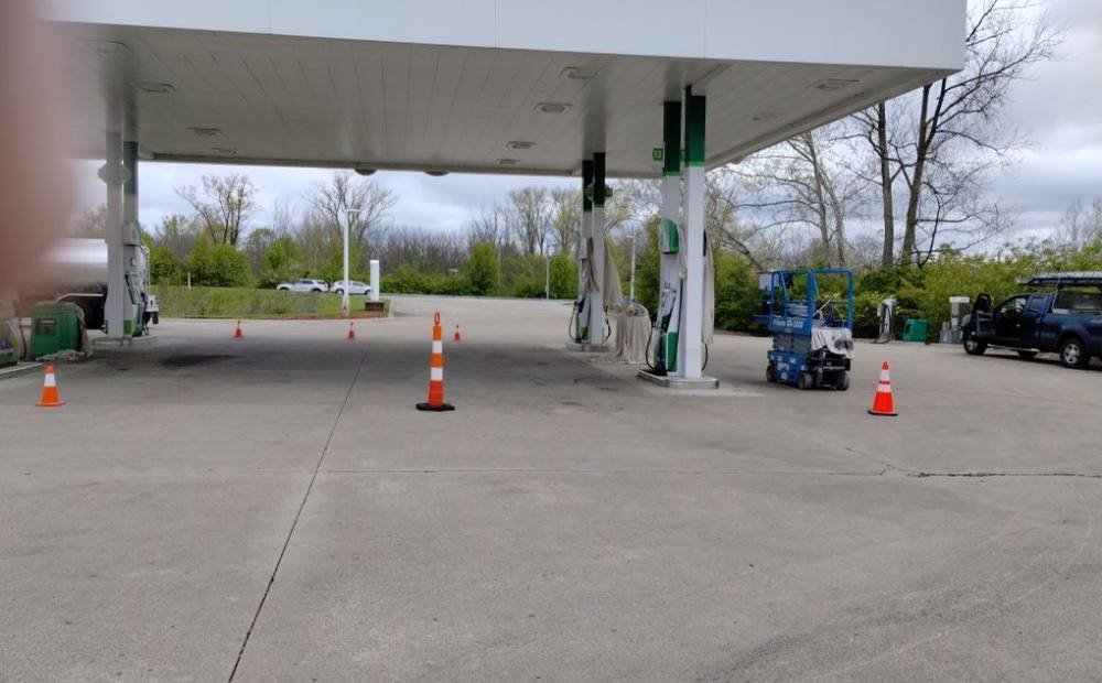 A freshly painted white and green service-station canopy with traffic cones on the forecourt below and bare trees behind.