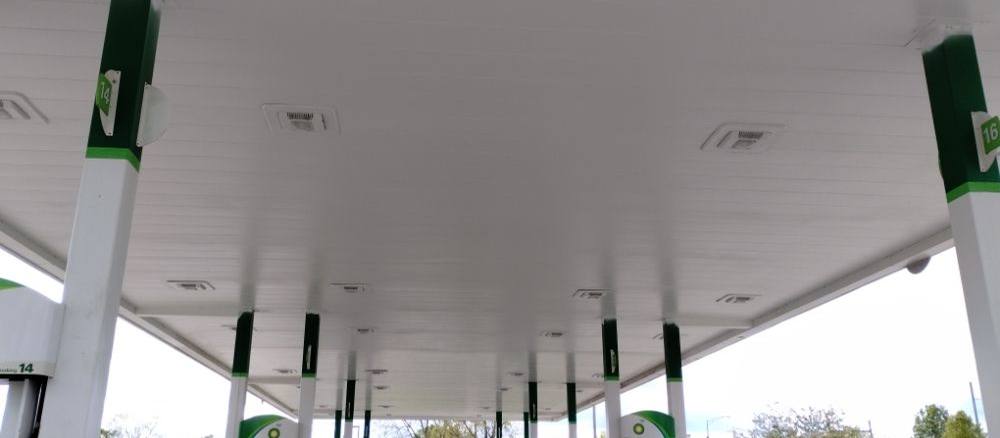 The white painted underside of a service-station canopy running the full width of the forecourt.